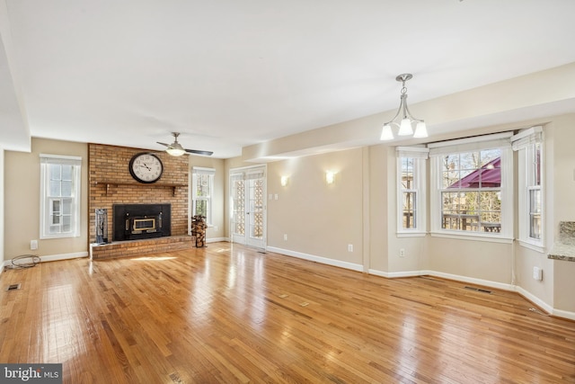 unfurnished living room featuring a ceiling fan, baseboards, visible vents, light wood finished floors, and a brick fireplace