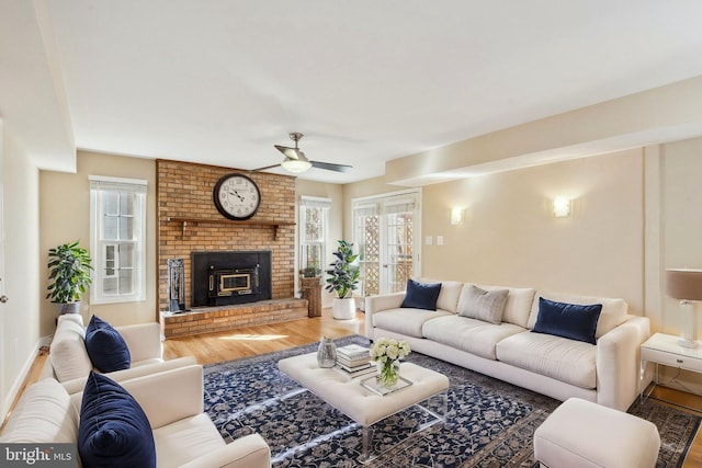 living area featuring a fireplace, ceiling fan, wood finished floors, and a healthy amount of sunlight