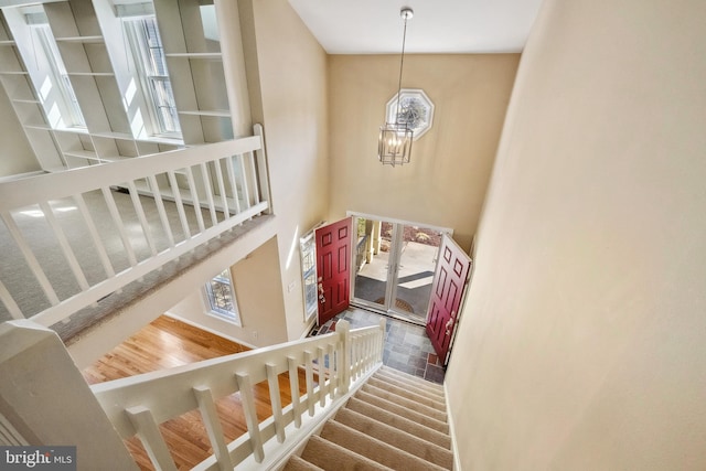 staircase with an inviting chandelier, a towering ceiling, and wood finished floors