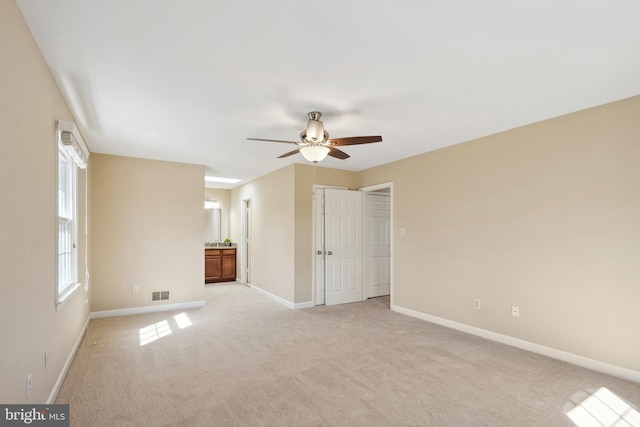 unfurnished bedroom featuring visible vents, ensuite bathroom, a ceiling fan, baseboards, and light colored carpet