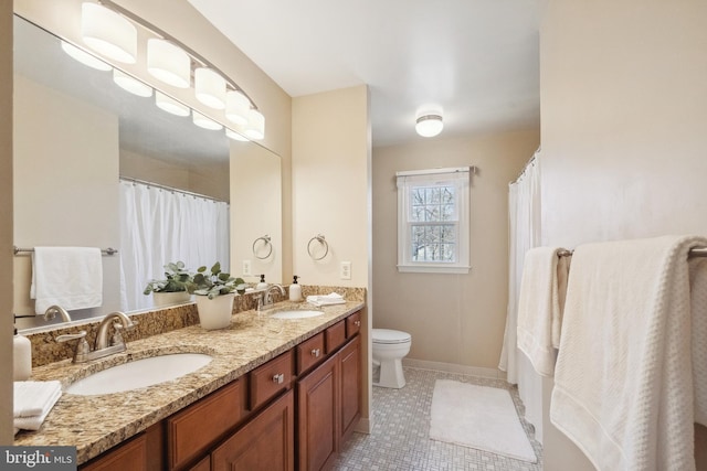 bathroom with double vanity, toilet, baseboards, and a sink