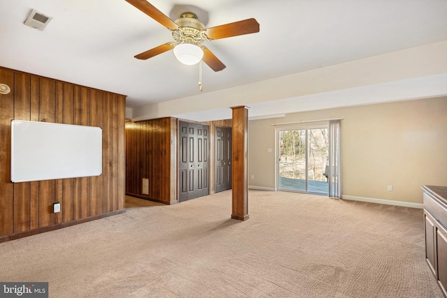 unfurnished living room with light carpet, wooden walls, baseboards, and visible vents