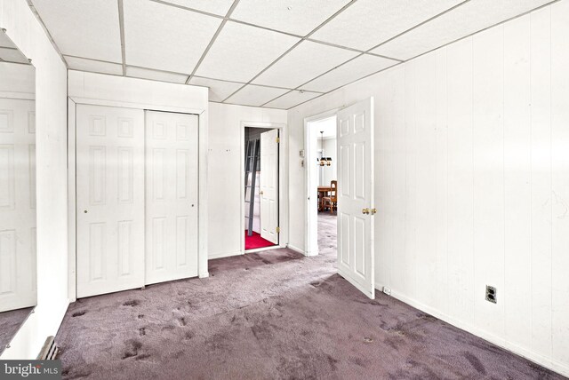 unfurnished bedroom with baseboards, a paneled ceiling, carpet floors, and a closet