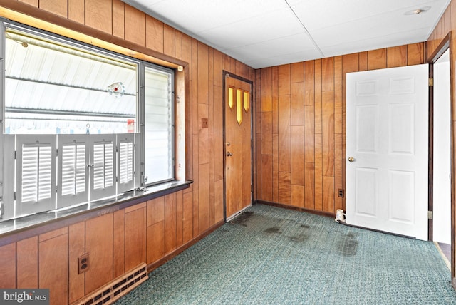 foyer entrance featuring wood walls and dark colored carpet