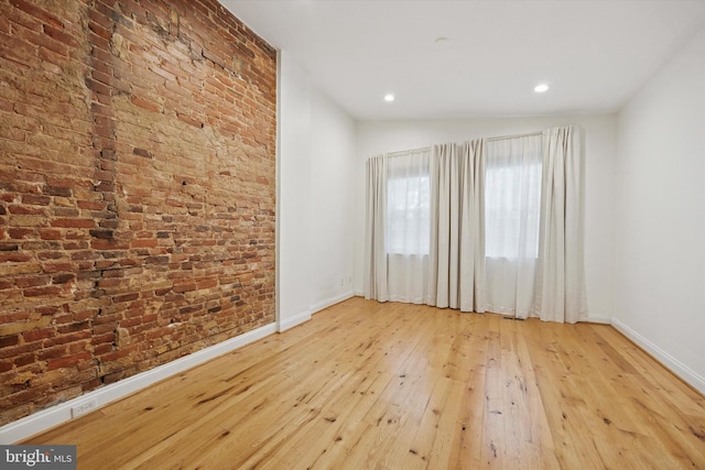 spare room featuring brick wall, baseboards, lofted ceiling, recessed lighting, and wood-type flooring