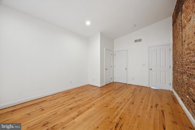 spare room with visible vents, high vaulted ceiling, brick wall, light wood finished floors, and baseboards