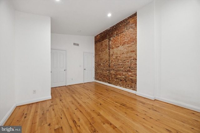 spare room featuring visible vents, brick wall, baseboards, and hardwood / wood-style floors