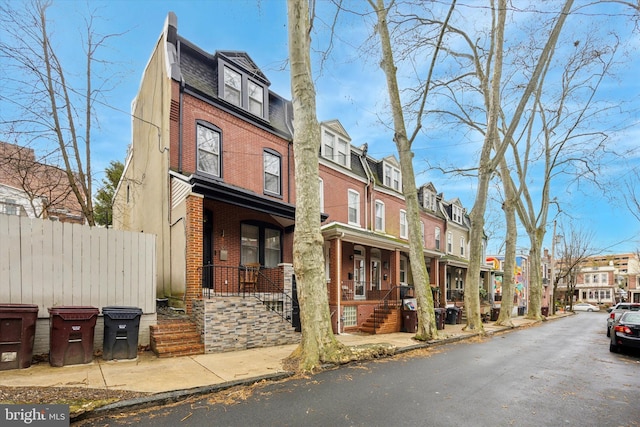 view of property with a porch, mansard roof, brick siding, and a residential view