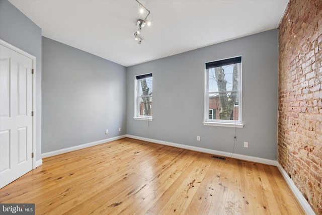 spare room with visible vents, wood-type flooring, baseboards, and brick wall