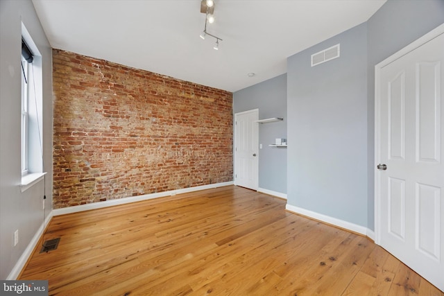 spare room featuring visible vents, hardwood / wood-style floors, and brick wall