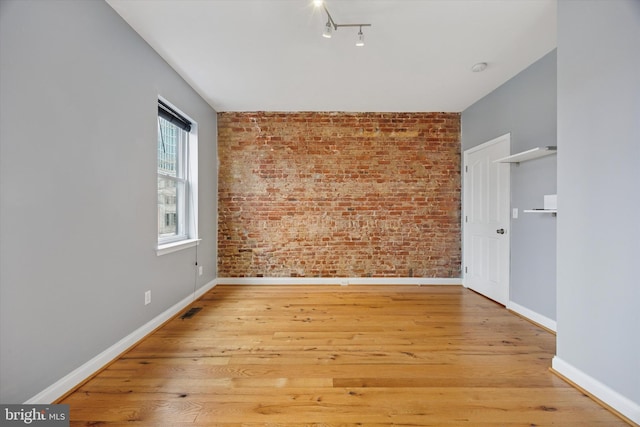 unfurnished room featuring visible vents, light wood-style flooring, brick wall, and baseboards