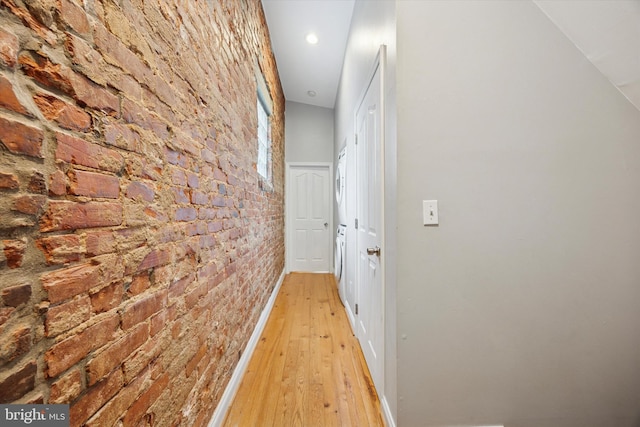 hallway with washer / clothes dryer, light wood-style floors, baseboards, and brick wall