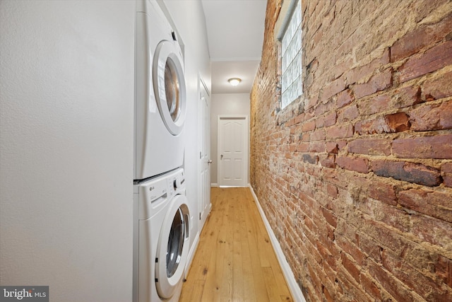 laundry room featuring baseboards, light wood finished floors, brick wall, laundry area, and stacked washer and dryer