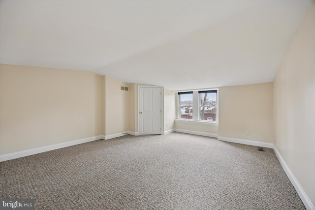 carpeted spare room featuring baseboards and vaulted ceiling