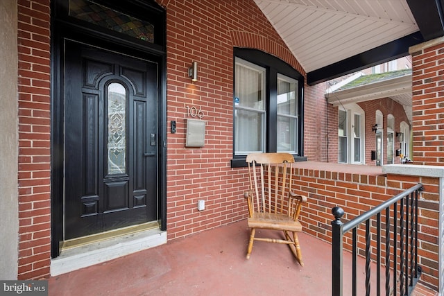 doorway to property with a porch and brick siding