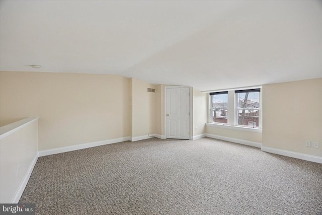 carpeted spare room featuring vaulted ceiling, visible vents, and baseboards