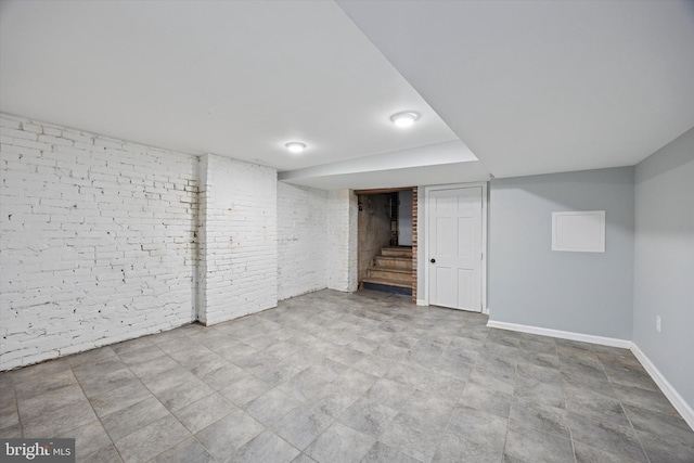 finished basement featuring baseboards, brick wall, and stairs