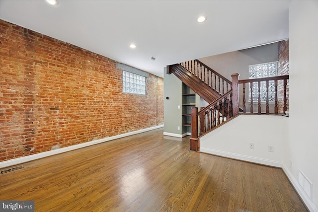 unfurnished room featuring wood finished floors, visible vents, brick wall, and baseboards