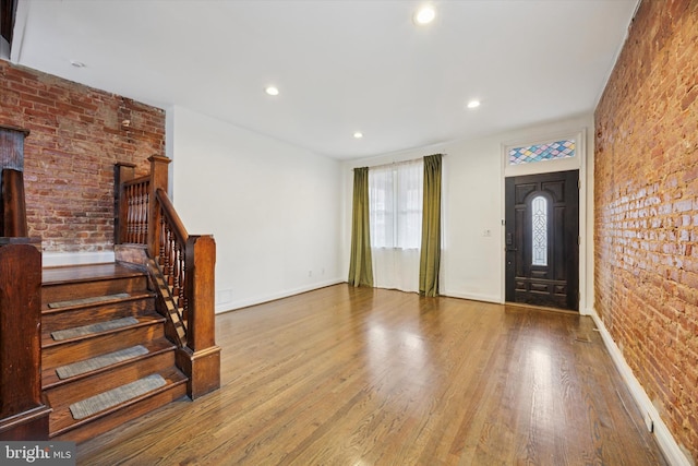 foyer entrance featuring stairway, wood finished floors, baseboards, and brick wall