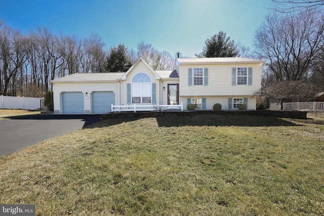 tri-level home featuring a garage, driveway, a front yard, and fence