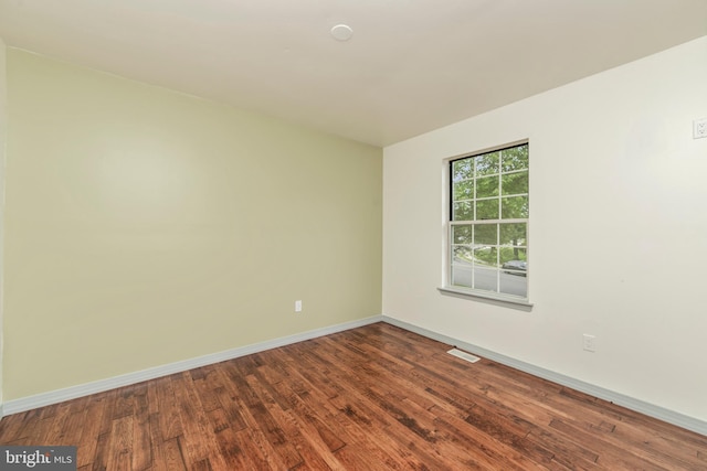 empty room featuring dark wood-style flooring, visible vents, and baseboards