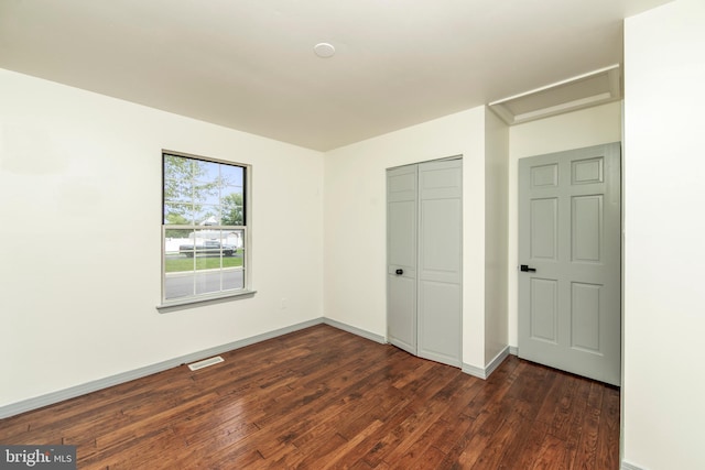 unfurnished bedroom with baseboards, visible vents, dark wood finished floors, and a closet