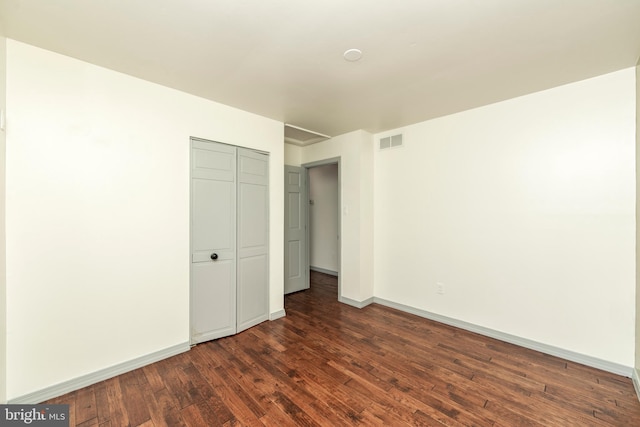 unfurnished bedroom with dark wood-style floors, a closet, visible vents, and baseboards