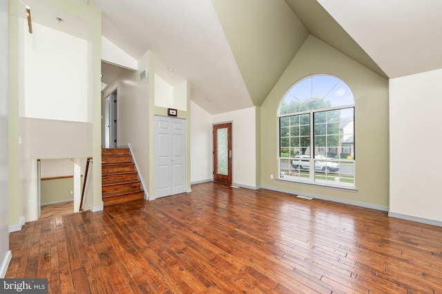 unfurnished living room featuring visible vents, stairway, high vaulted ceiling, baseboards, and hardwood / wood-style flooring