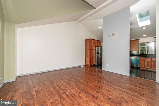 unfurnished living room featuring vaulted ceiling with skylight, recessed lighting, a sink, baseboards, and dark wood-style floors