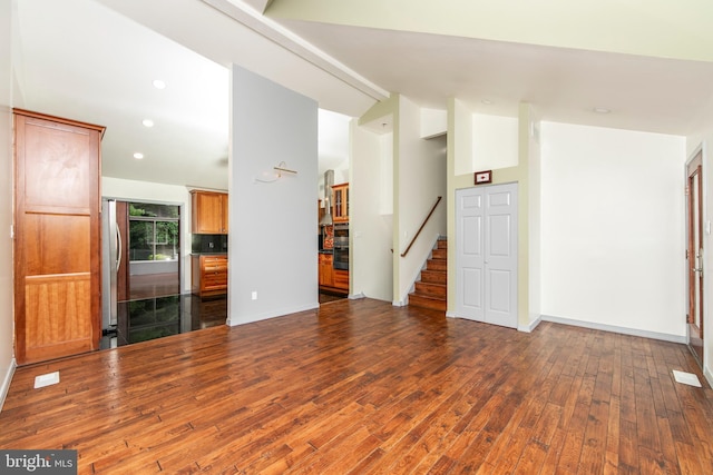 unfurnished living room featuring baseboards, stairway, vaulted ceiling, and hardwood / wood-style floors