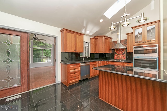 kitchen featuring vaulted ceiling with skylight, wall chimney exhaust hood, appliances with stainless steel finishes, granite finish floor, and backsplash