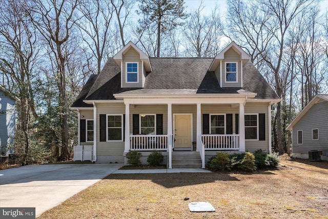 new england style home with a porch, a shingled roof, and cooling unit