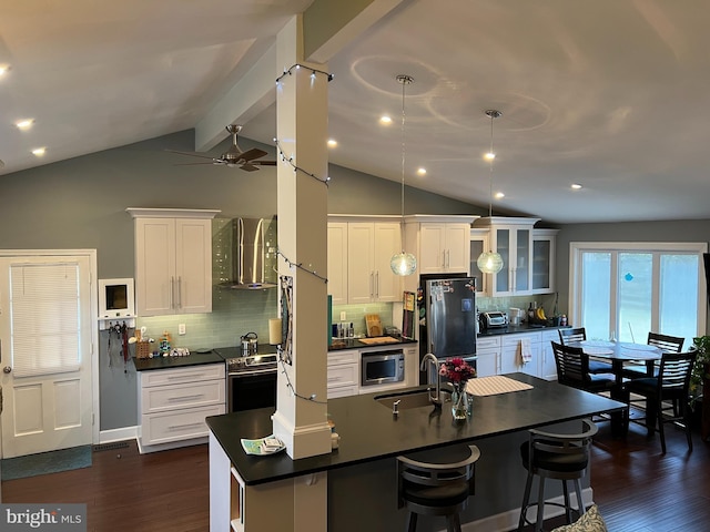 kitchen with a sink, appliances with stainless steel finishes, white cabinetry, dark countertops, and wall chimney exhaust hood