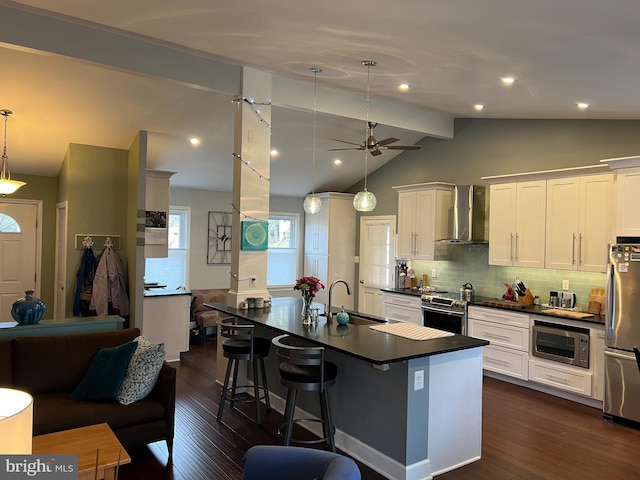 kitchen featuring dark countertops, dark wood-type flooring, wall chimney range hood, appliances with stainless steel finishes, and a sink