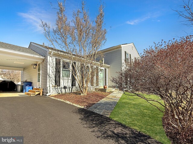 view of side of property with aphalt driveway, an attached carport, and a lawn