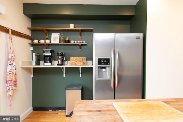 kitchen with stainless steel fridge, a kitchen bar, baseboards, and wood finished floors