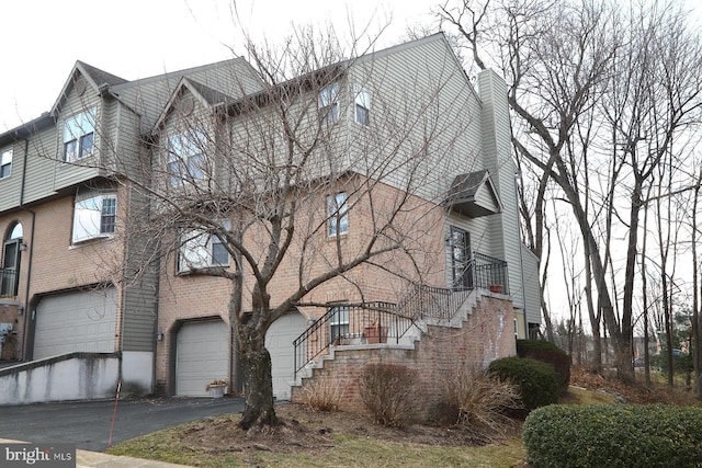 view of side of property with brick siding, a chimney, a garage, driveway, and stairs