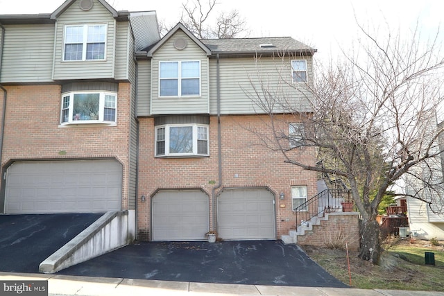 back of property with driveway, brick siding, an attached garage, and cooling unit