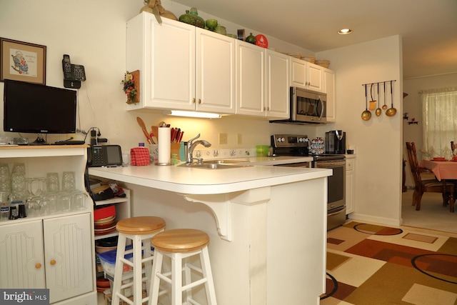 kitchen featuring a breakfast bar, appliances with stainless steel finishes, white cabinets, a sink, and a peninsula