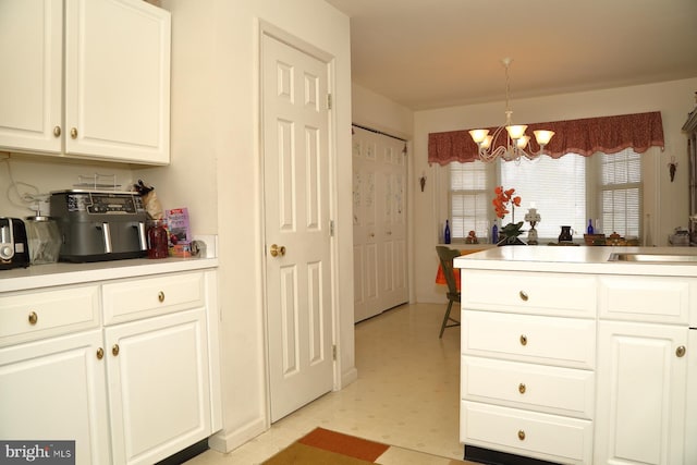 kitchen with a chandelier, light countertops, light floors, white cabinetry, and a sink