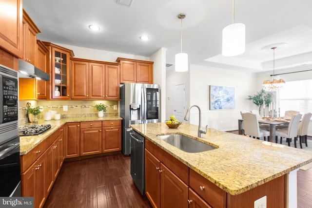 kitchen with dark wood-style floors, stainless steel appliances, brown cabinetry, a sink, and under cabinet range hood