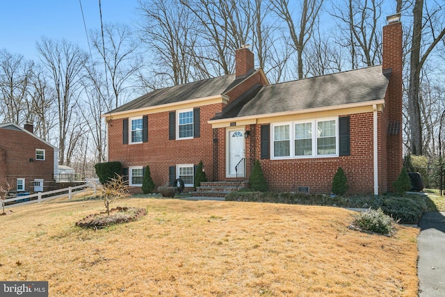 split level home featuring a front yard, fence, brick siding, and a chimney