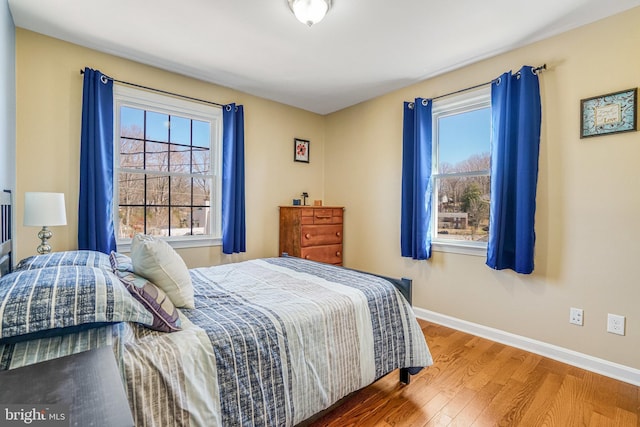 bedroom with multiple windows, wood finished floors, and baseboards