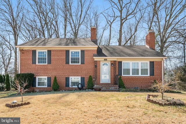 split level home with brick siding, entry steps, a chimney, and a front lawn