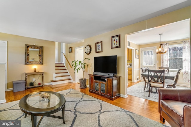 living area with a notable chandelier, stairway, baseboards, and wood finished floors