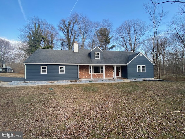 view of front of home featuring brick siding, a chimney, a porch, and a front lawn