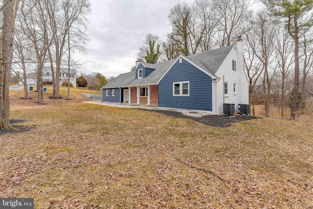 rear view of property with a chimney, central AC, and brick siding