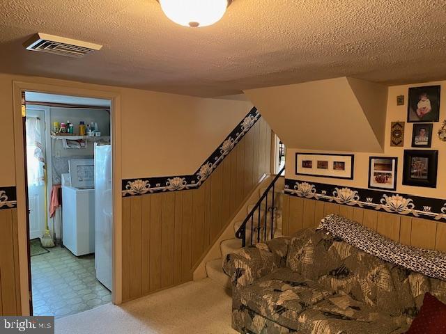 stairway with washer / clothes dryer, visible vents, wainscoting, wood walls, and a textured ceiling