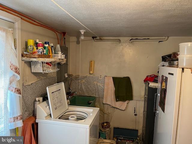 clothes washing area featuring a textured ceiling, laundry area, washer / clothes dryer, and a sink