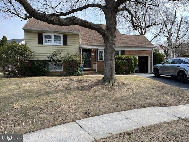 tri-level home with a garage, driveway, a shingled roof, and brick siding